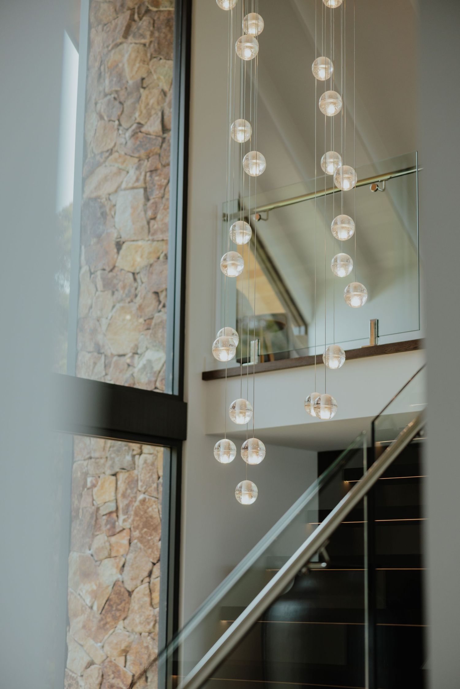 Modern home interior featuring a cascading globe chandelier beside a stone wall.
