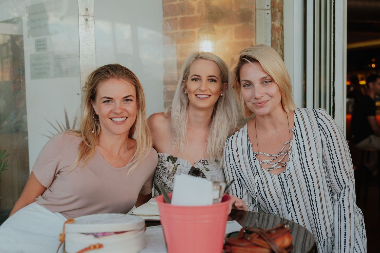 Three smiling blonde women seated together at a casual restaurant dining table.