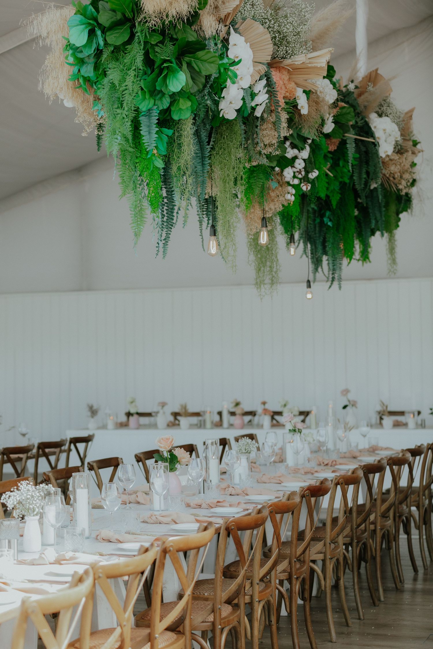 Stunning wedding reception with lush hanging floral installation above long rustic wooden dining tables.