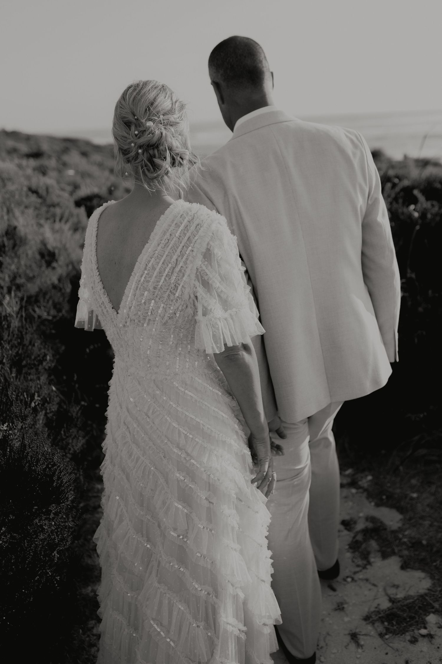 Black and white photo of bride in sequined fringe dress and groom walking hand in hand.