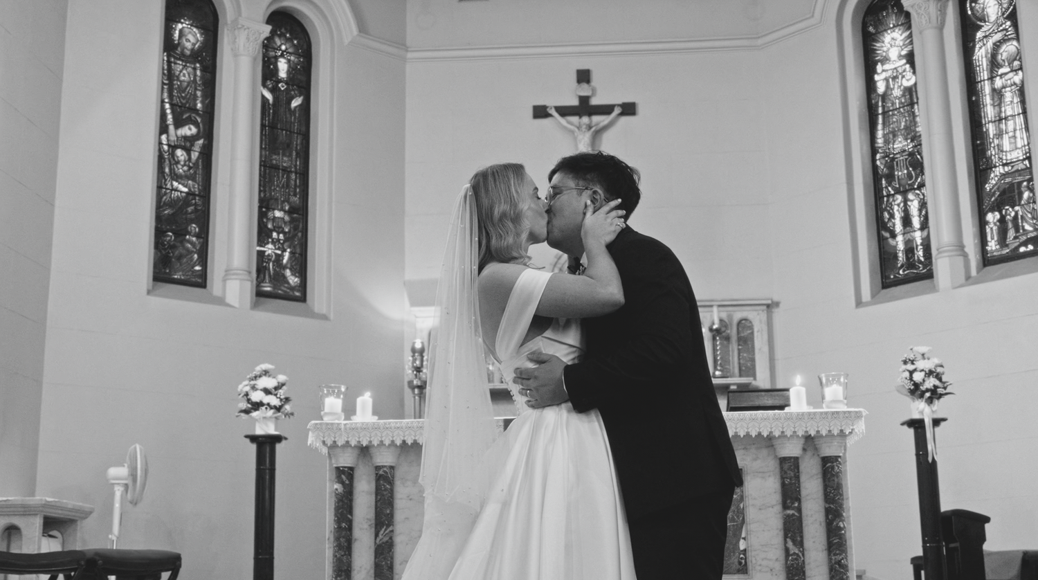 Black and white photo of couple sharing first kiss at church altar.