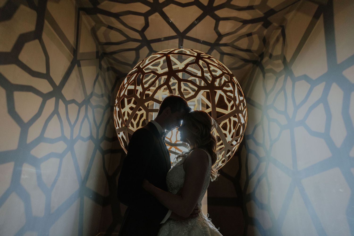 Silhouette of a couple embracing in front of a glowing geometric circular light installation.