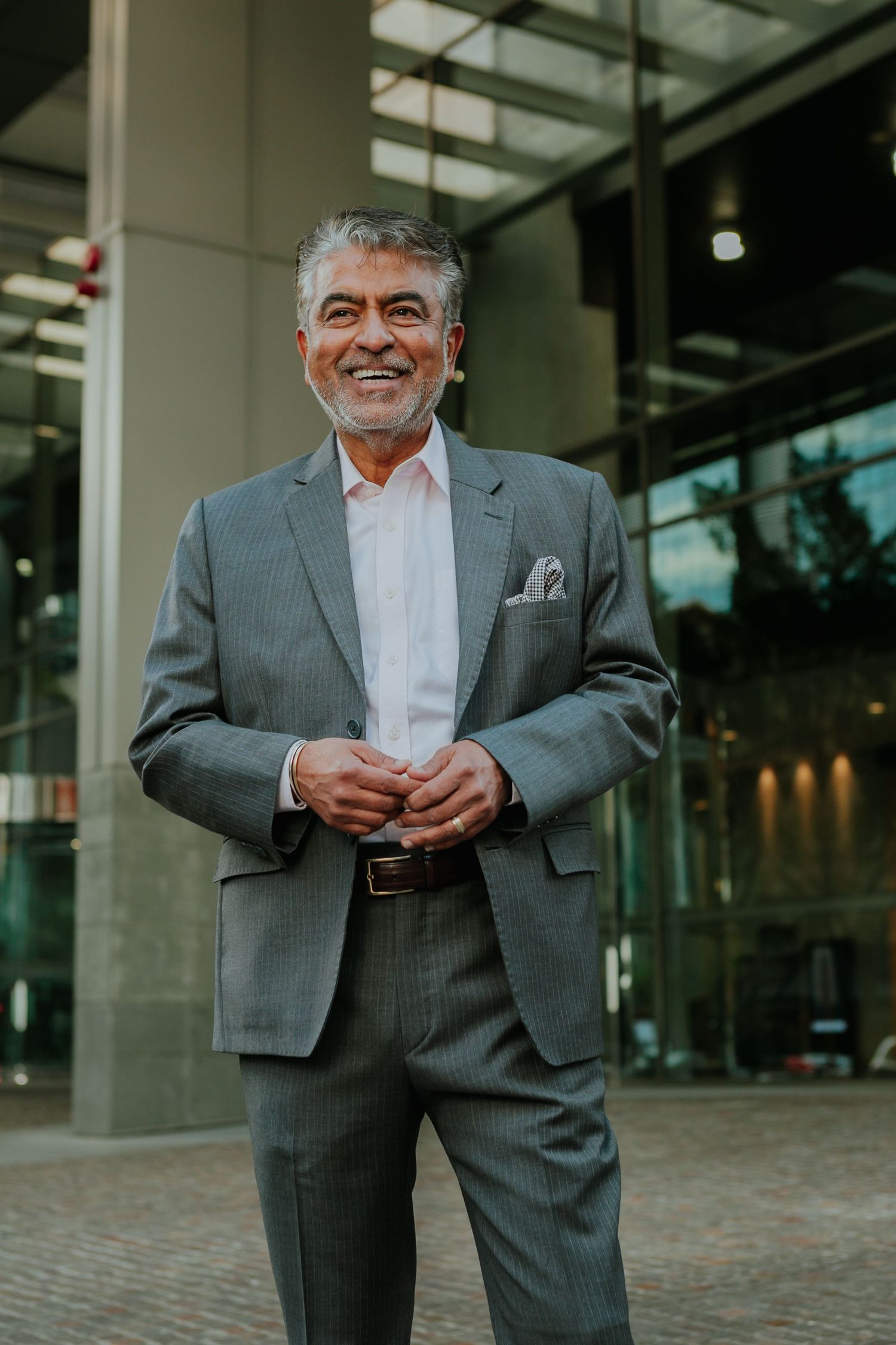 Confident senior businessman in gray suit smiling outside a modern glass building.