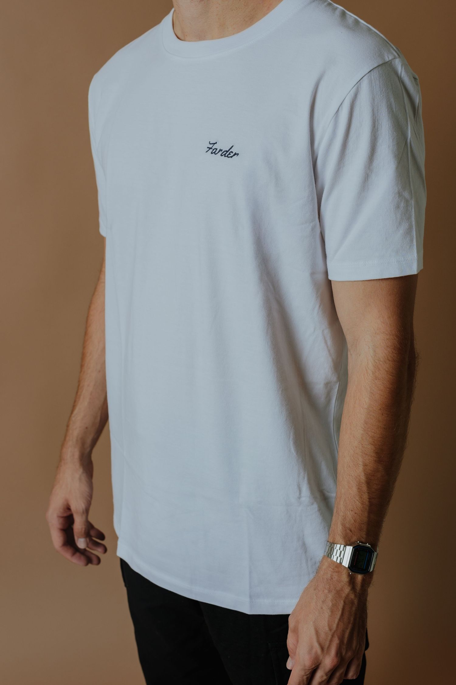 Side view of a man in a white t-shirt with embroidered script logo and black pants with a silver watch.