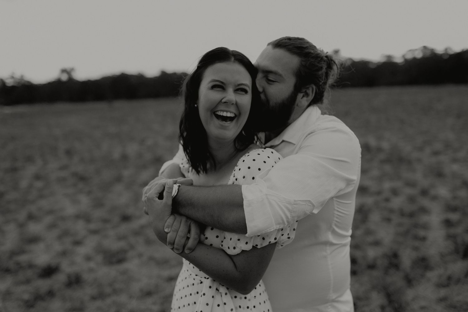 Black and white photo of a couple laughing and embracing in an open field.