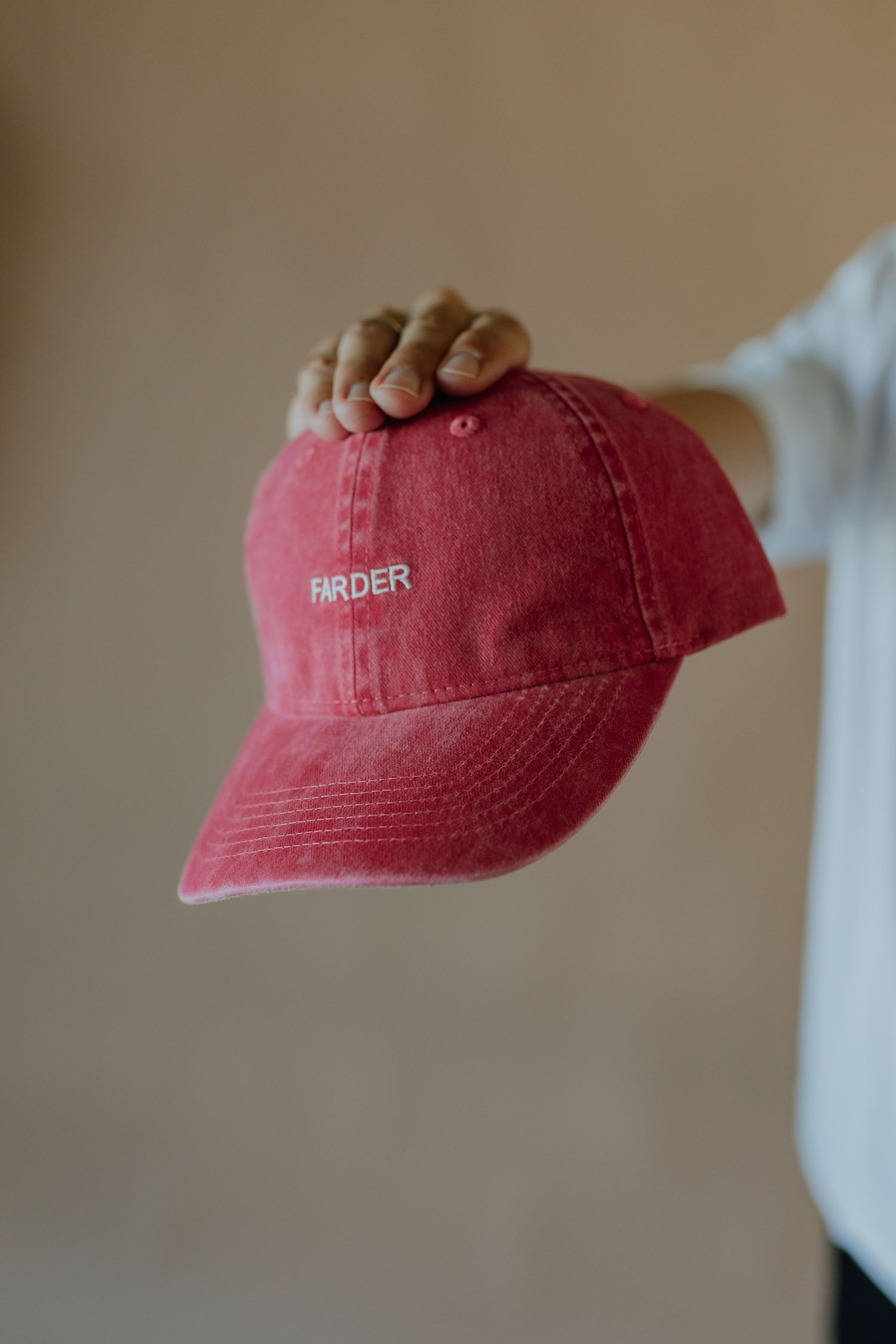 Hand holding a red distressed dad cap with white FARDER embroidered logo.
