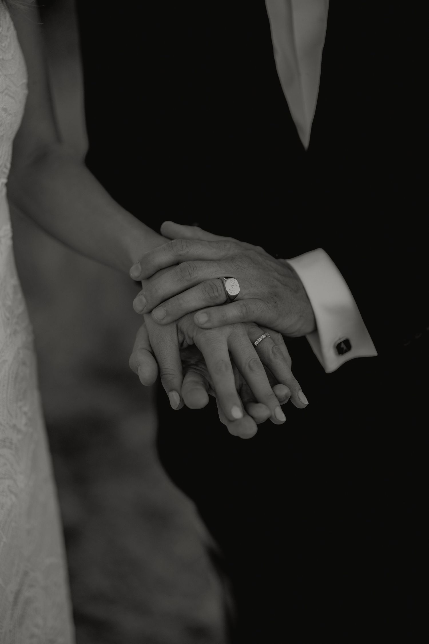Black and white close-up of bride and groom holding hands showing wedding rings and cufflinks.