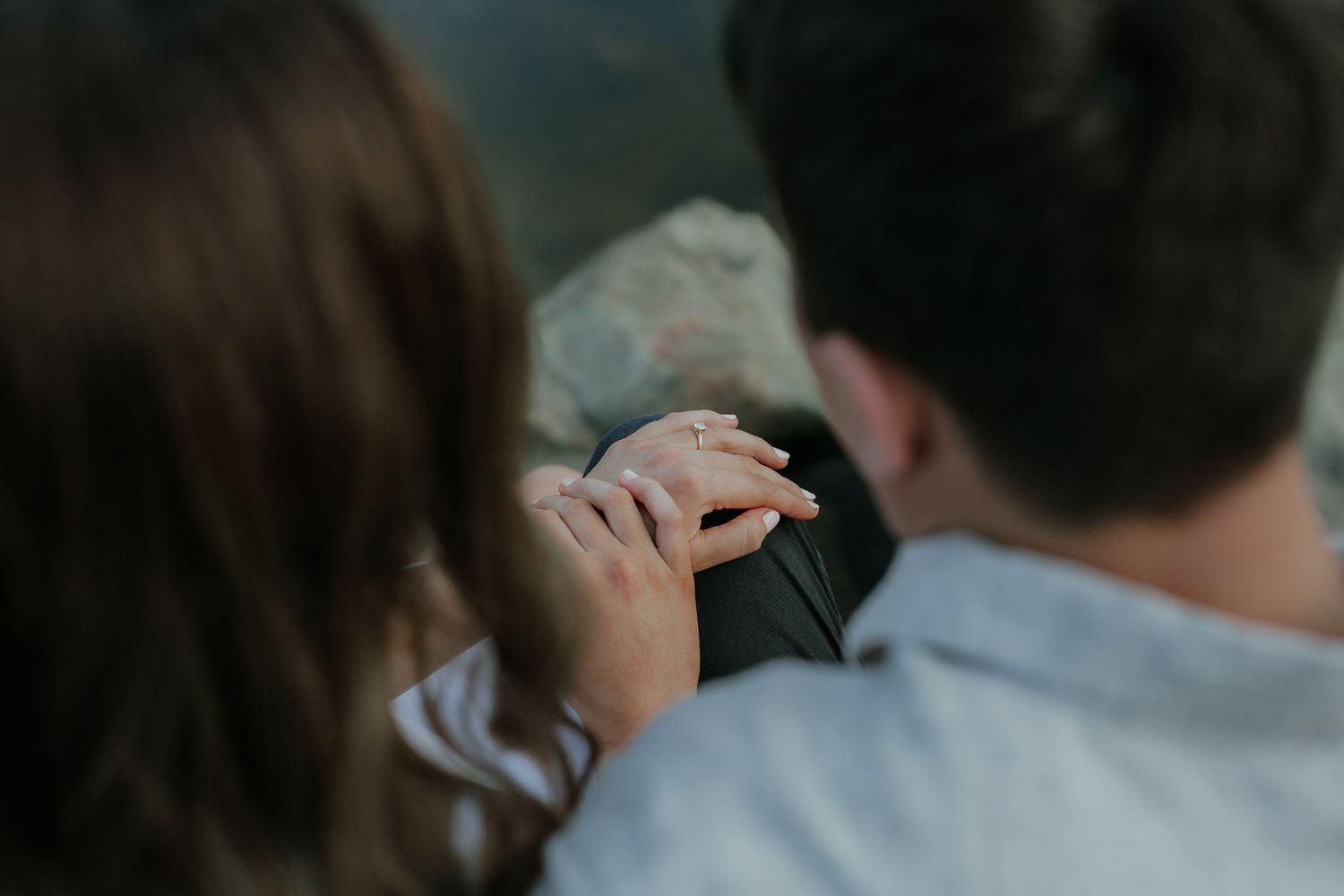 Close-up of a couple gently holding hands while sitting together on a rock outdoors.