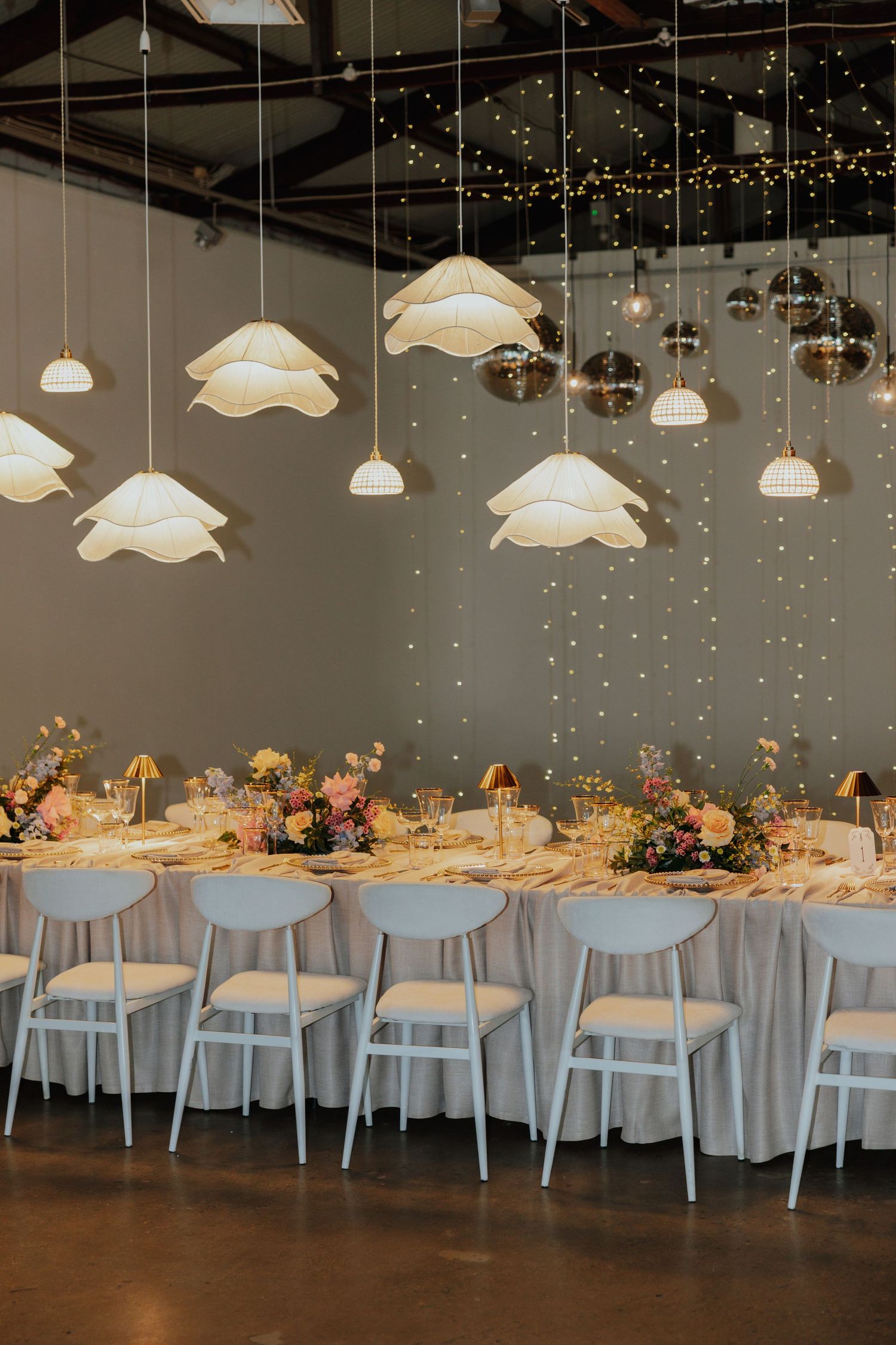 Dreamy wedding reception hall with cloud-shaped pendant lights, disco balls, fairy lights, and floral centerpieces.