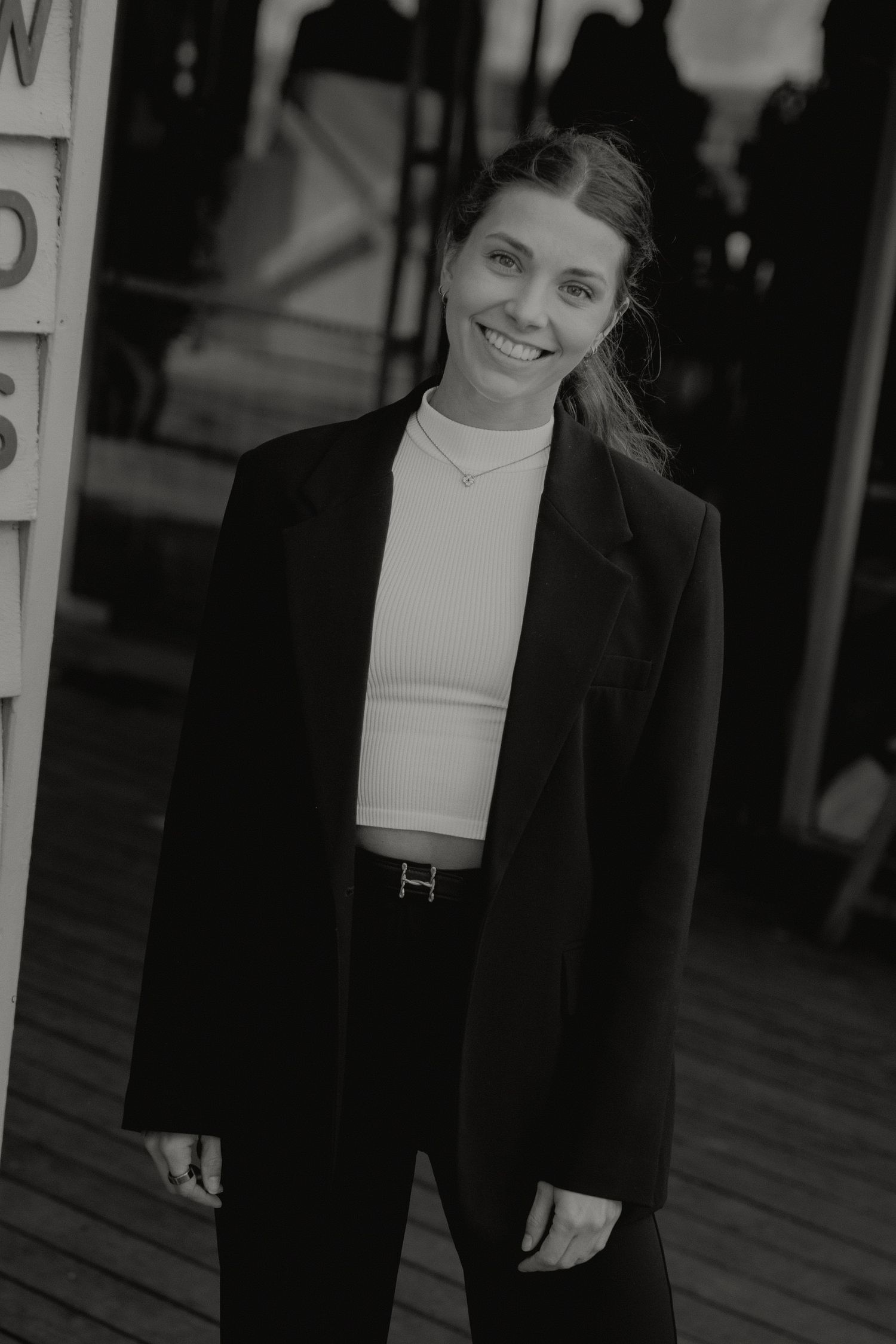 Smiling woman in black oversized blazer and white top posing outdoors in black and white.