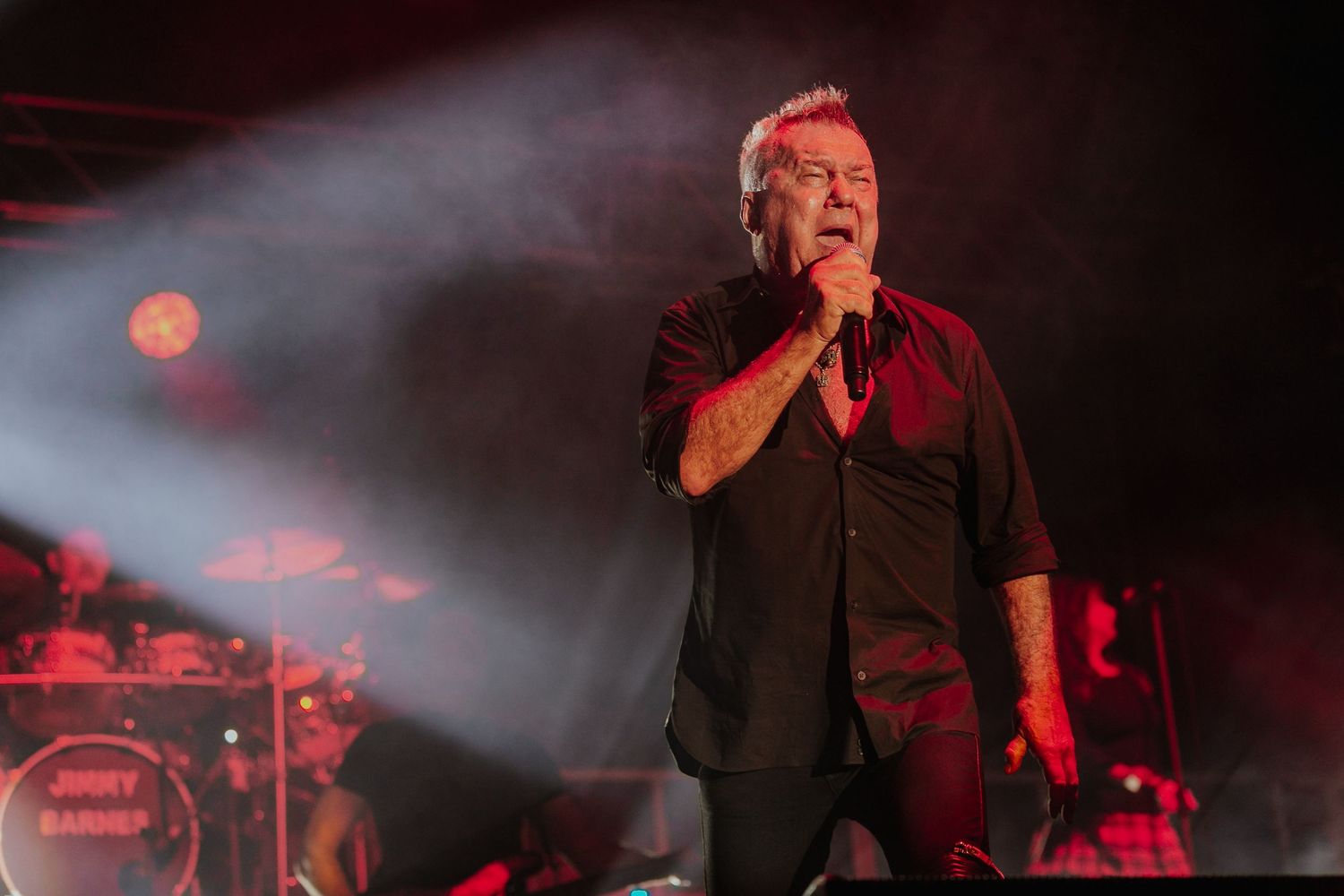 Tattooed male singer performing passionately on stage under red dramatic lighting at live concert.