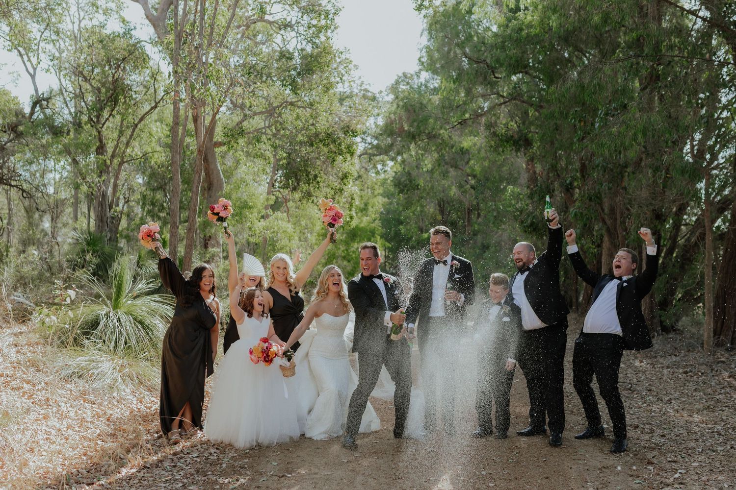 Wedding party celebrating with smoke bomb in a natural bush setting with raised bouquets.