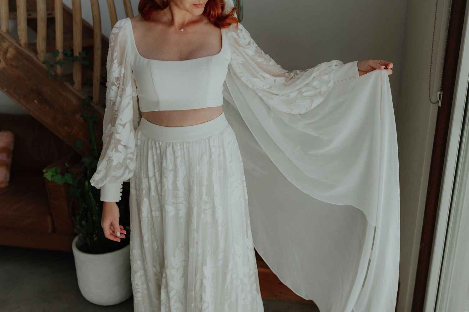Bride in white two-piece lace wedding gown with flowing bell sleeves posing indoors.