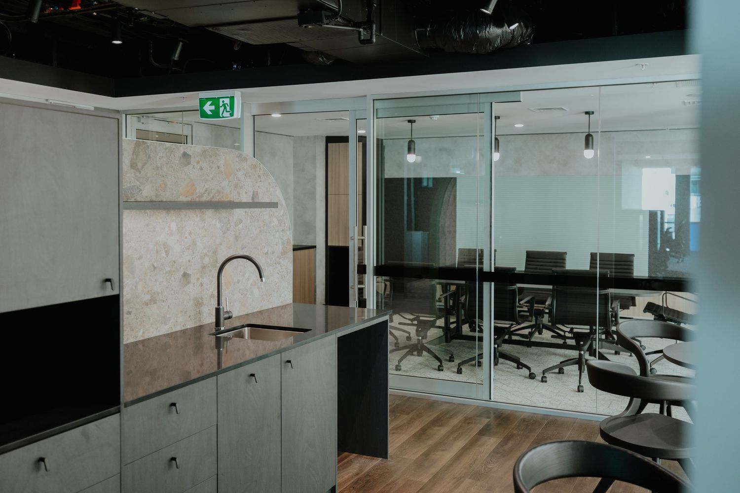 Modern office kitchenette with dark sink, grey cabinetry, and glass-walled conference room.