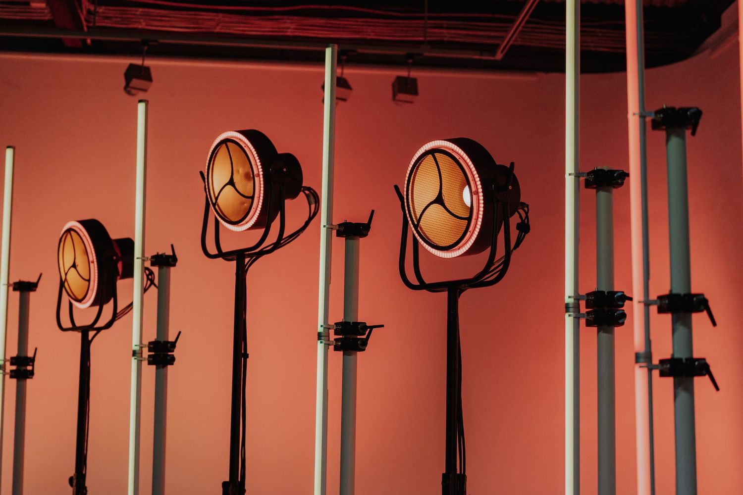 Vintage industrial stage spotlights mounted on poles against a warm pink wall.