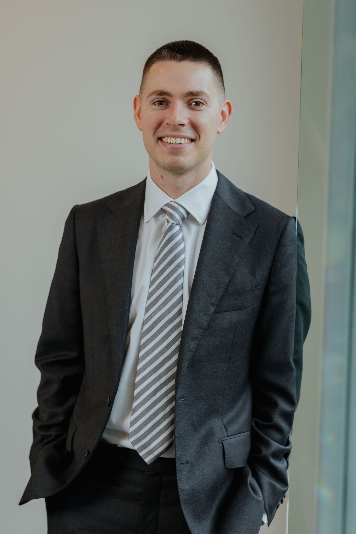 Confident young man in dark suit and striped tie smiling in a modern office.