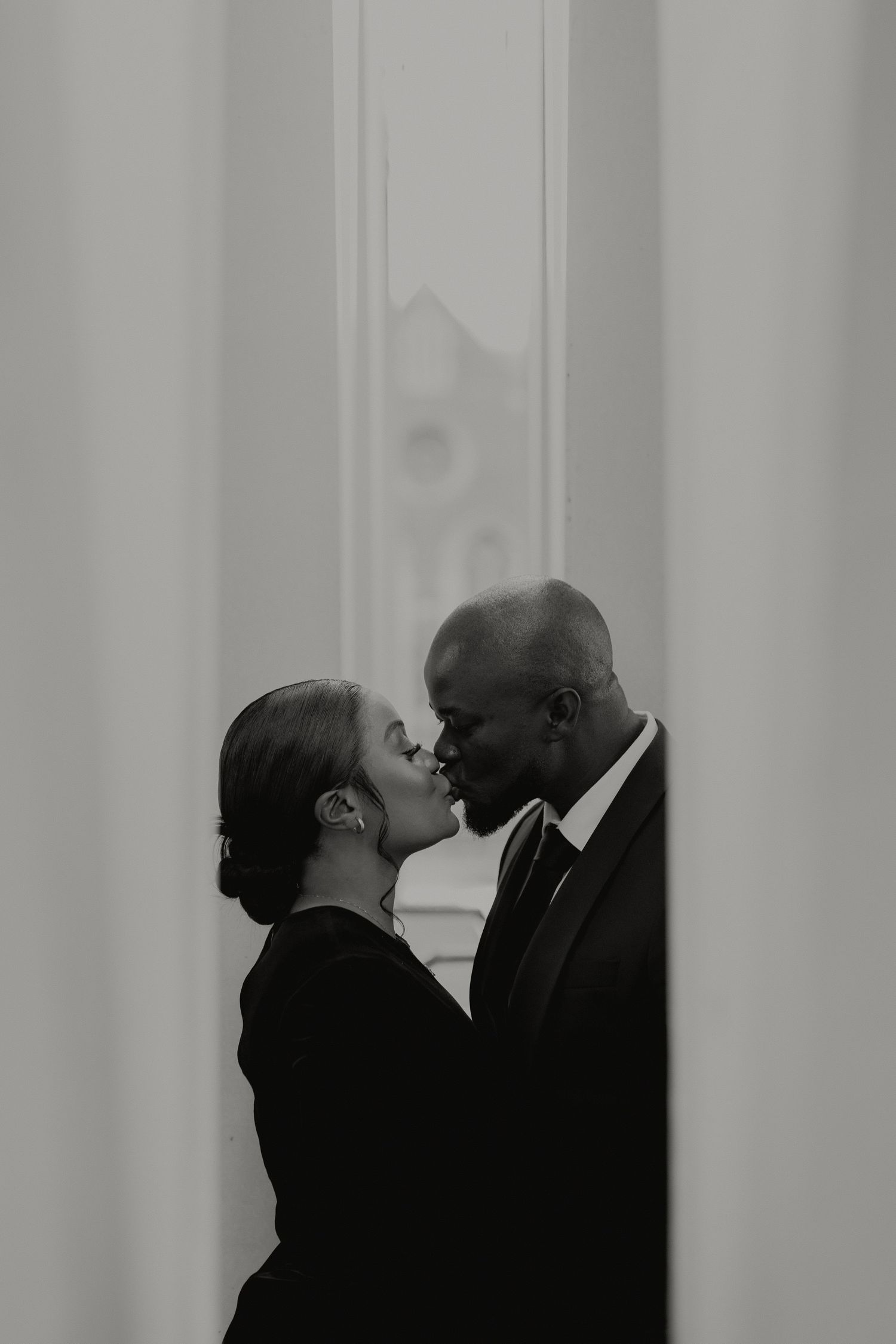 Black and white intimate portrait of interracial couple sharing a kiss indoors.