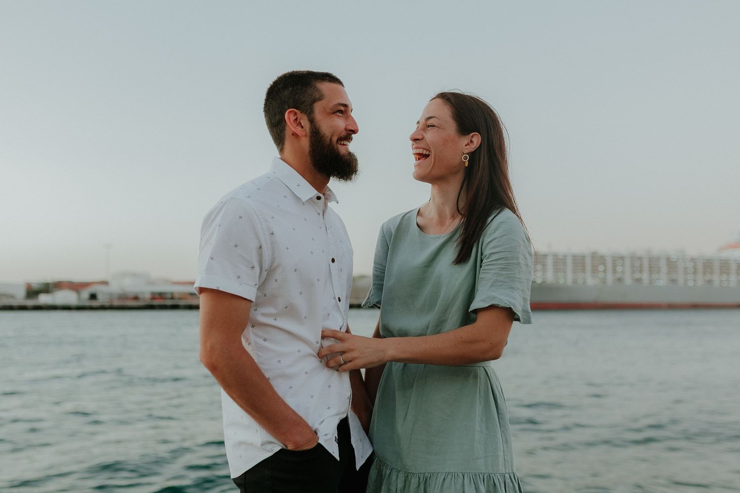 Laughing couple holding hands near the waterfront at dusk.