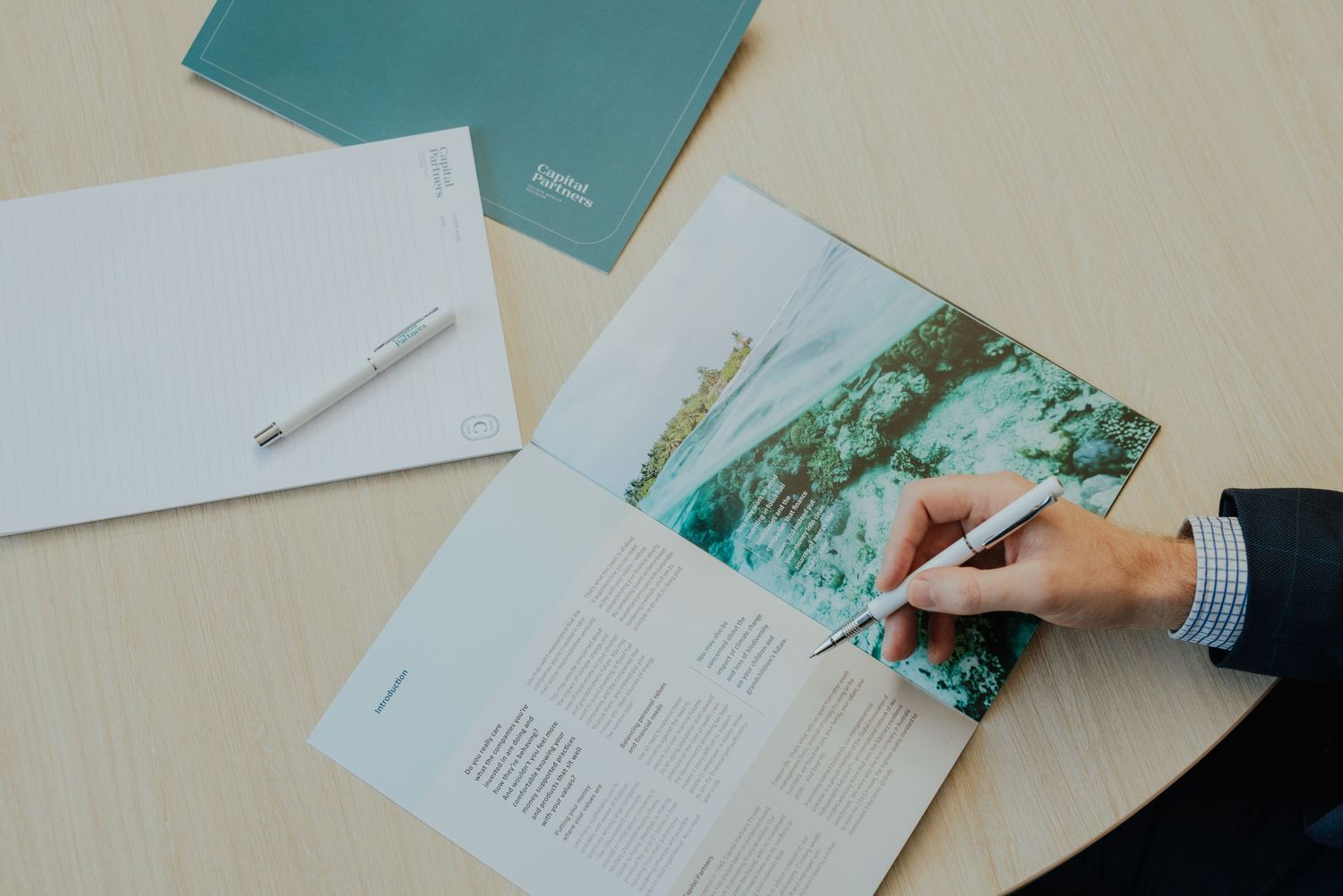 Professional reviewing a document with a pen on a desk with teal folders in a modern office setting.