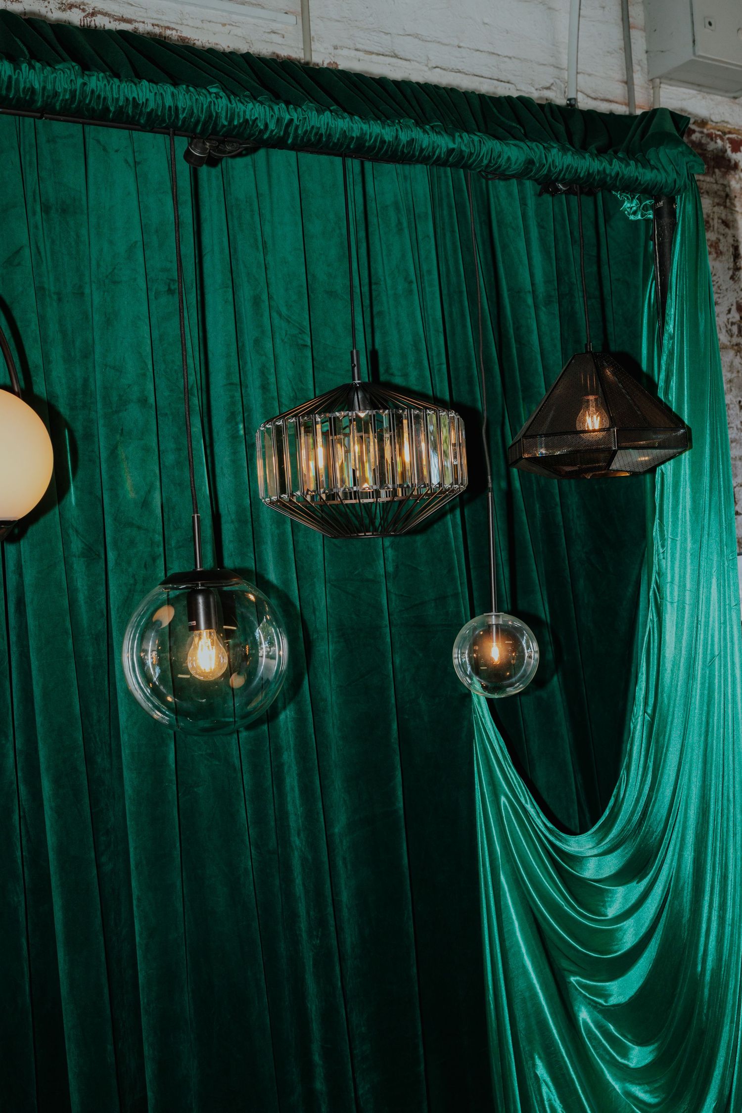 Assorted pendant lights hanging against emerald green velvet curtains in a stylish interior setting.