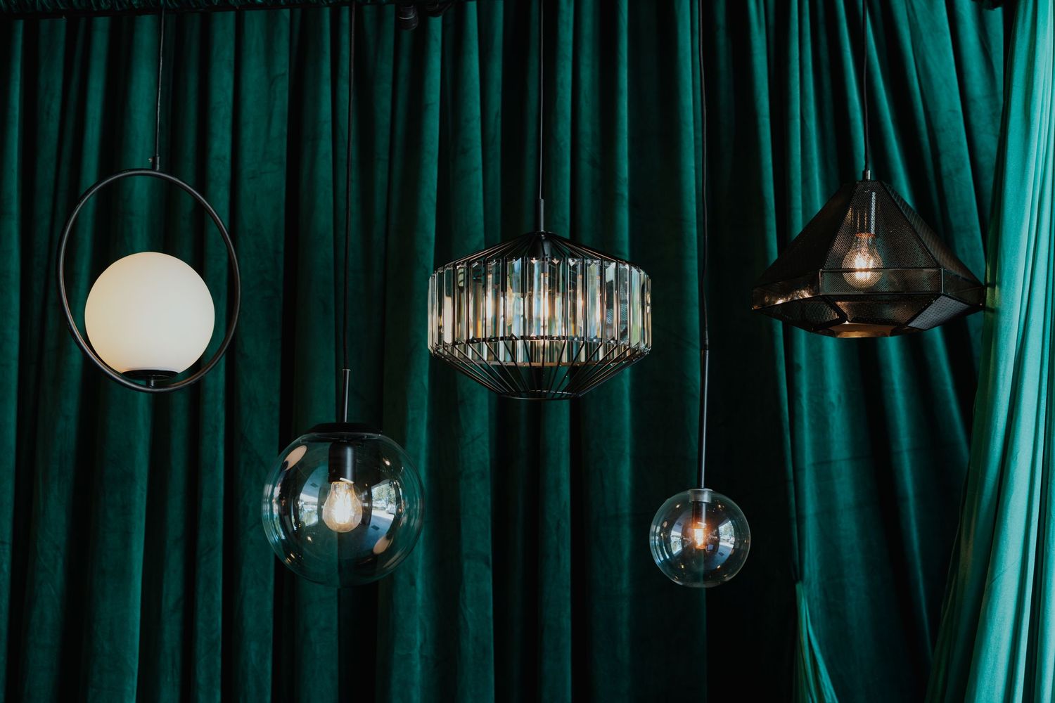 Assorted decorative pendant lights hanging against a rich emerald green velvet curtain backdrop.