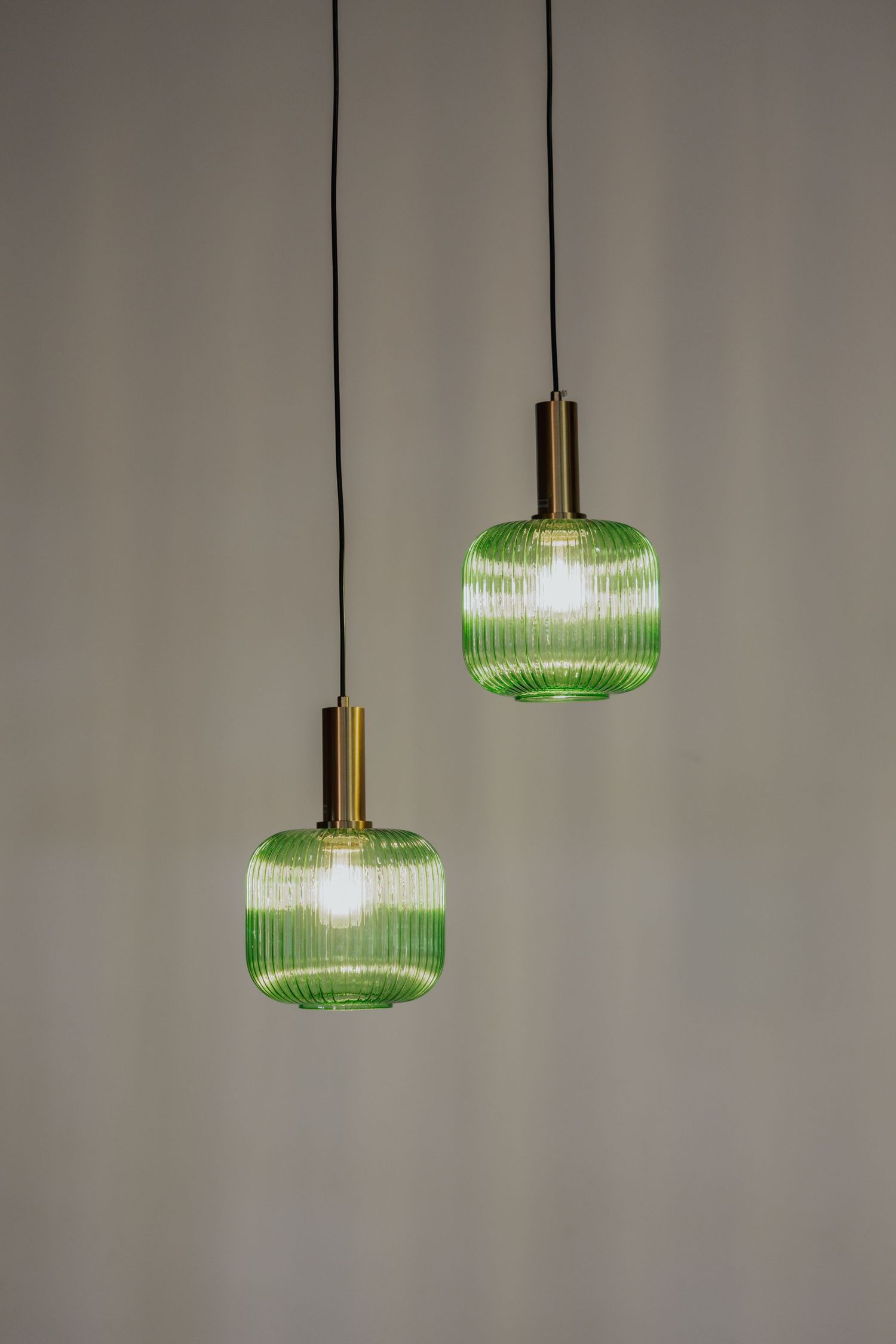 Pair of ribbed green glass pendant lights with brass fittings hanging against neutral gray background.