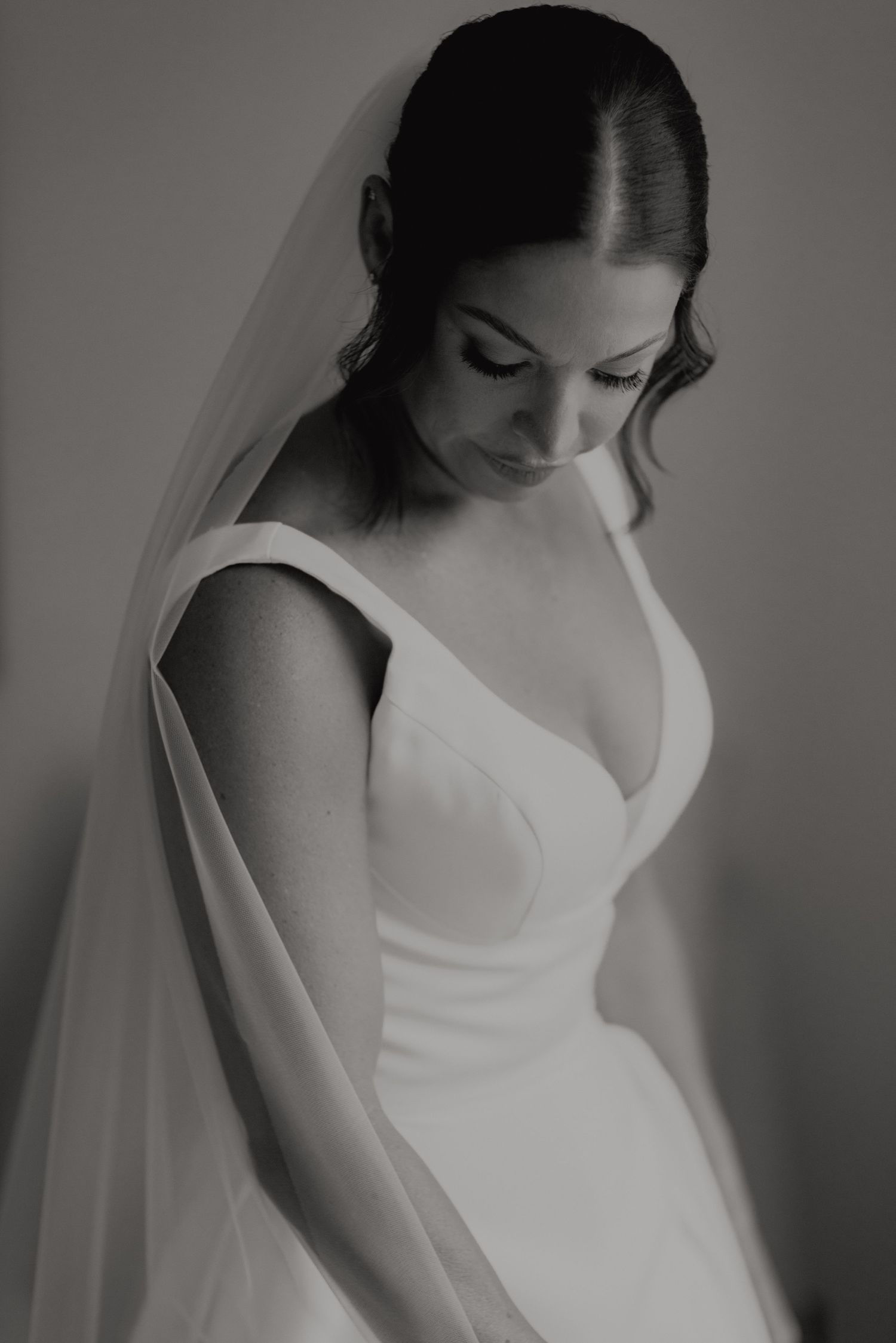 Elegant black and white portrait of bride in fitted gown and veil looking down softly.