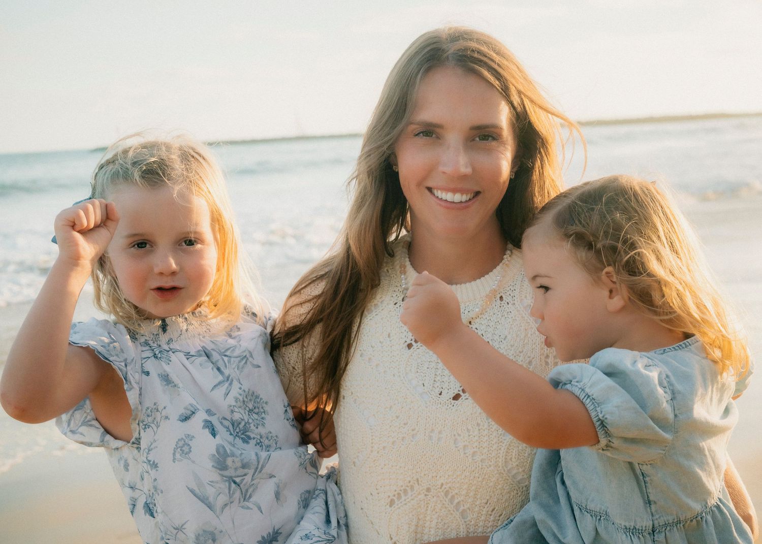Brunette mother posing with two young daughters flexing arms on sunny beach.