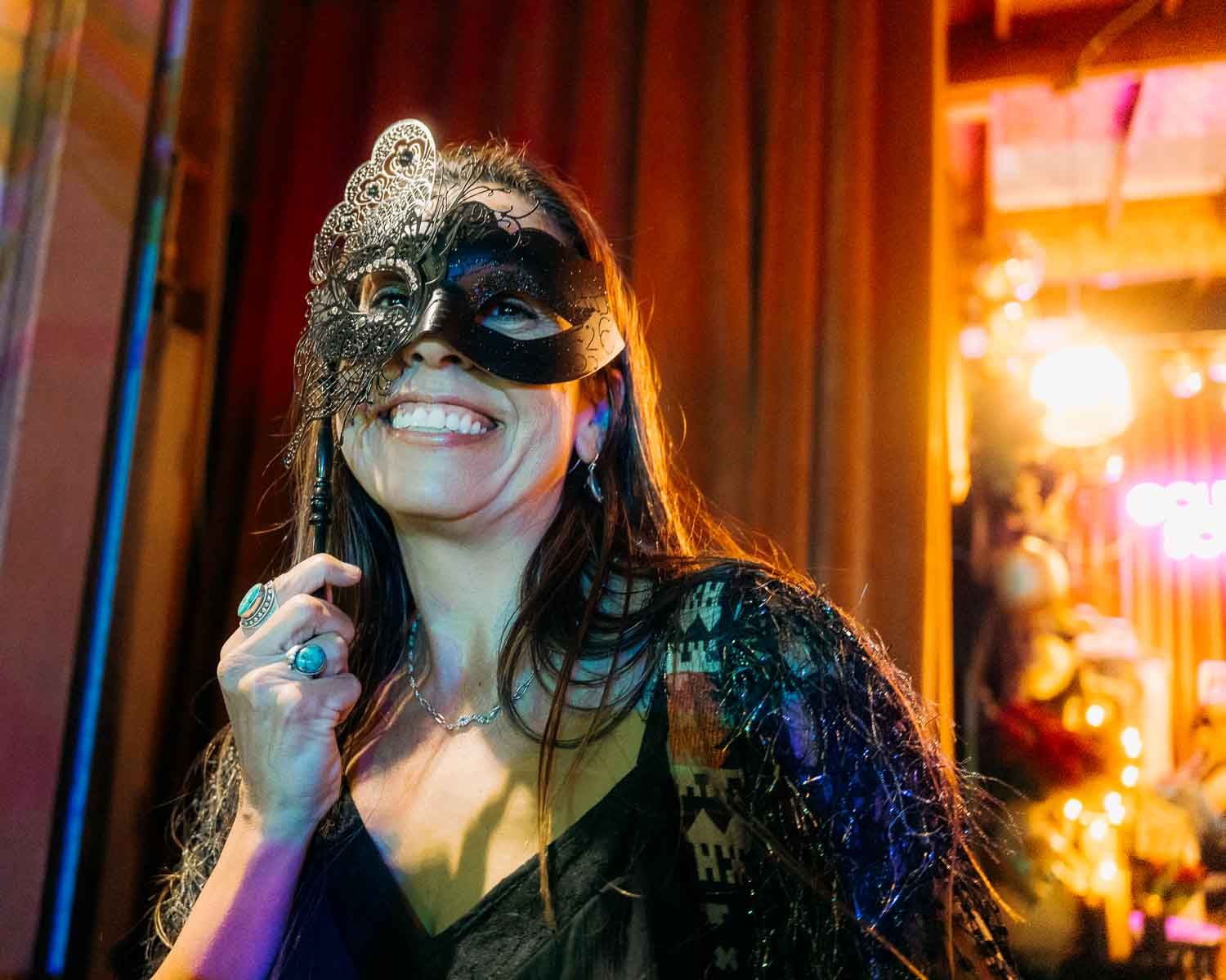 Woman in elegant masquerade mask smiling and posing at a festive masquerade party.