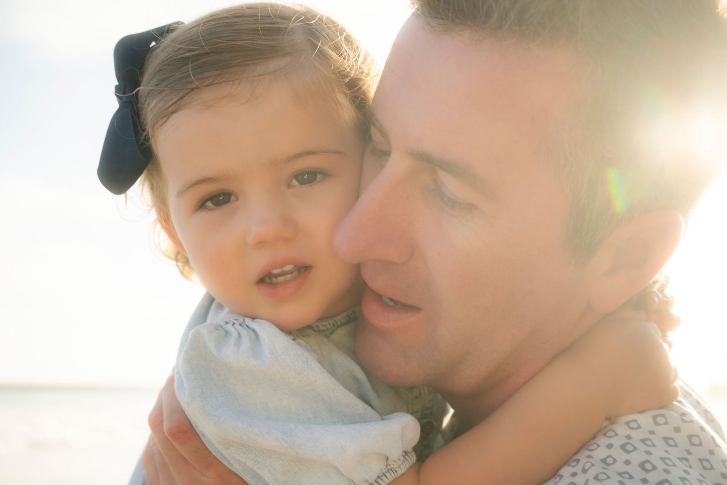 A father tenderly holds his baby girl close on a bright sunny beach.
