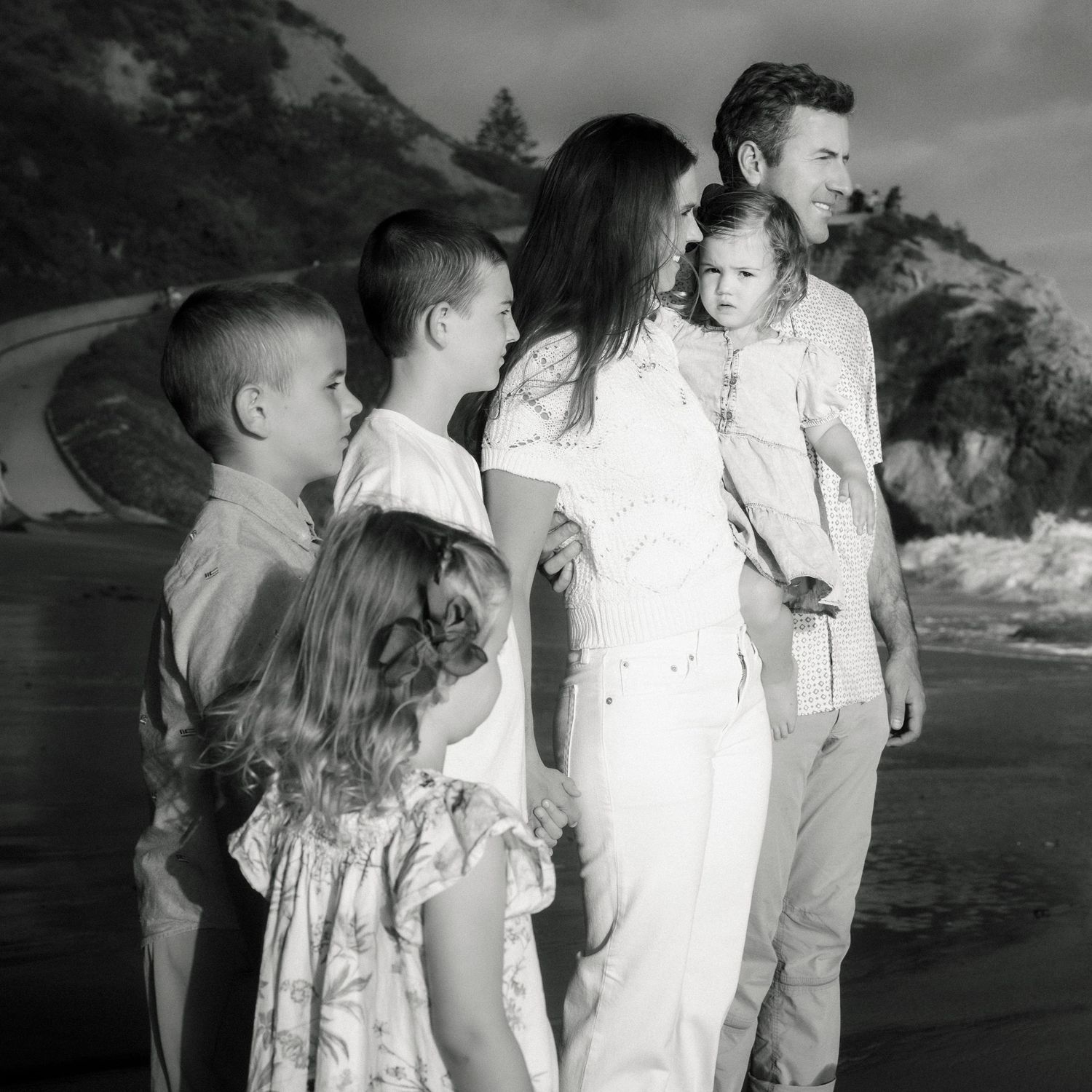 A black and white portrait of a family of six standing together on a rocky beach.
