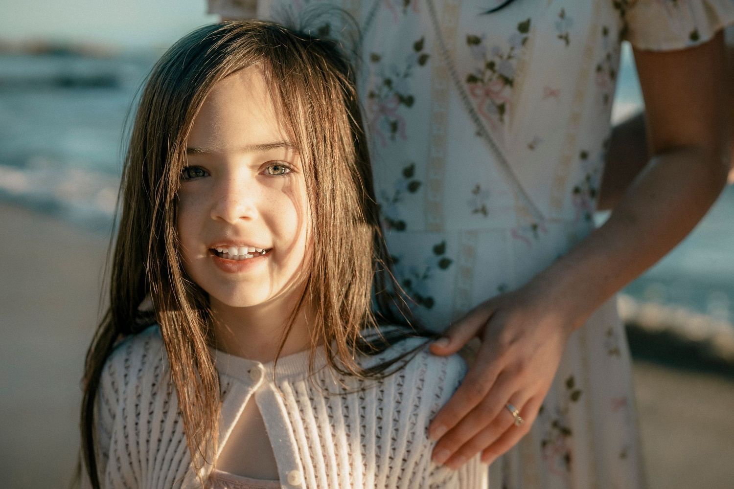 Young girl with long brown hair smiling warmly at beach during golden hour.
