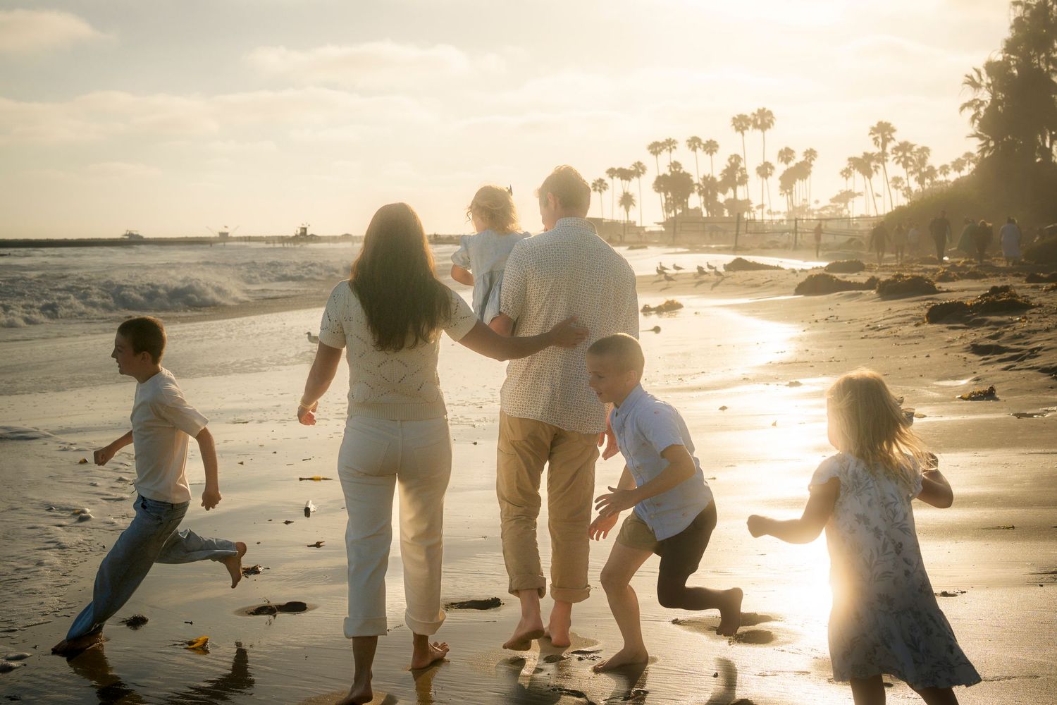 A family walks together along a scenic beach at sunset with children playing nearby.