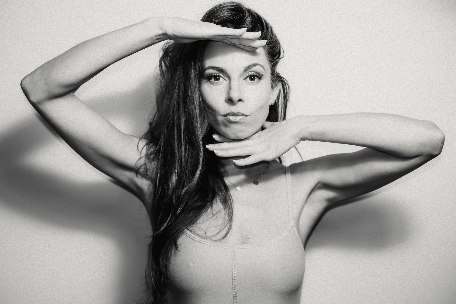 Black and white portrait of a woman with long dark hair posing with hands framing her face.