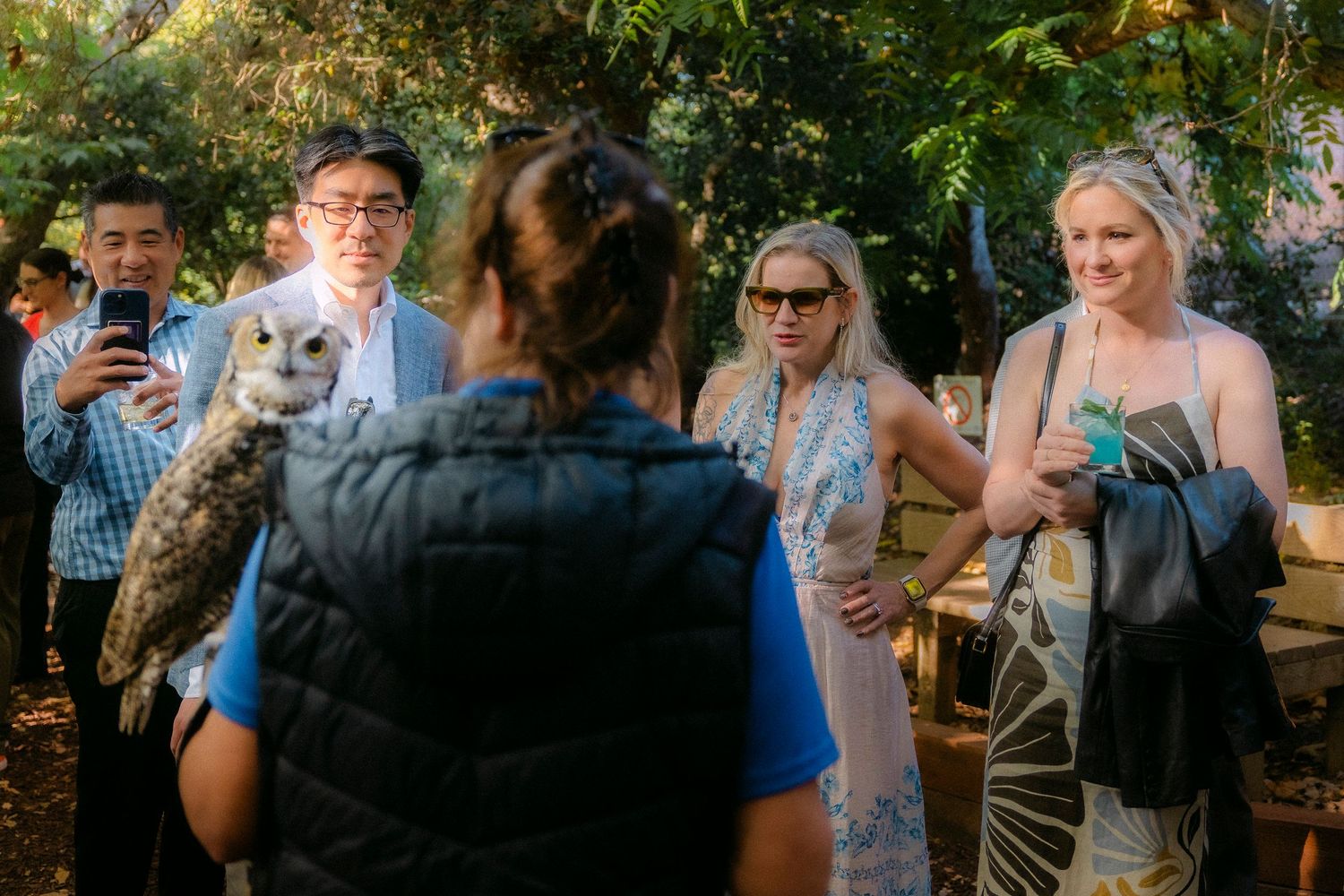 Wildlife handler shows a barn owl to curious guests at an elegant outdoor garden gathering.