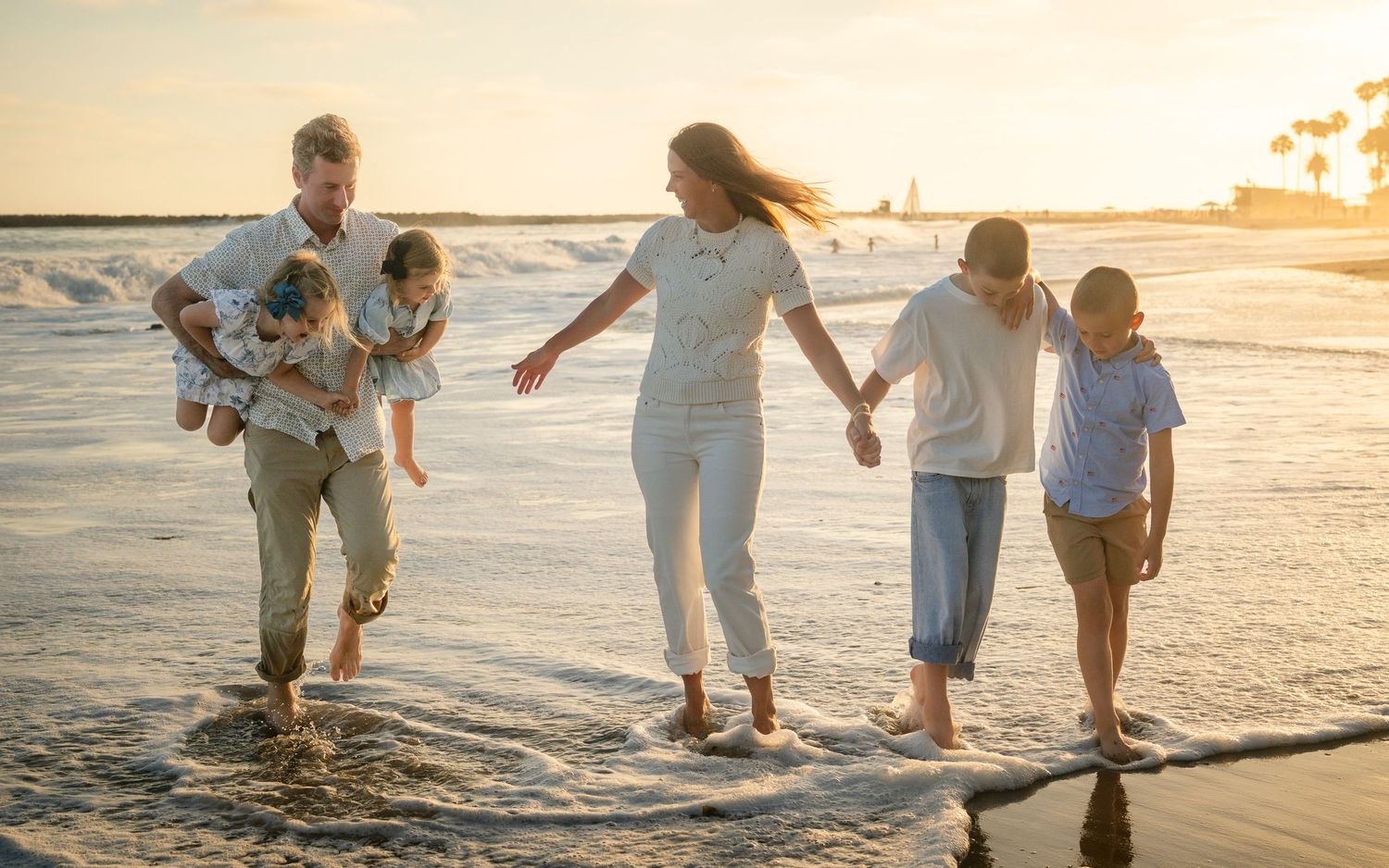 Extended family of six walking along a sunny beach shoreline at golden sunset hour.