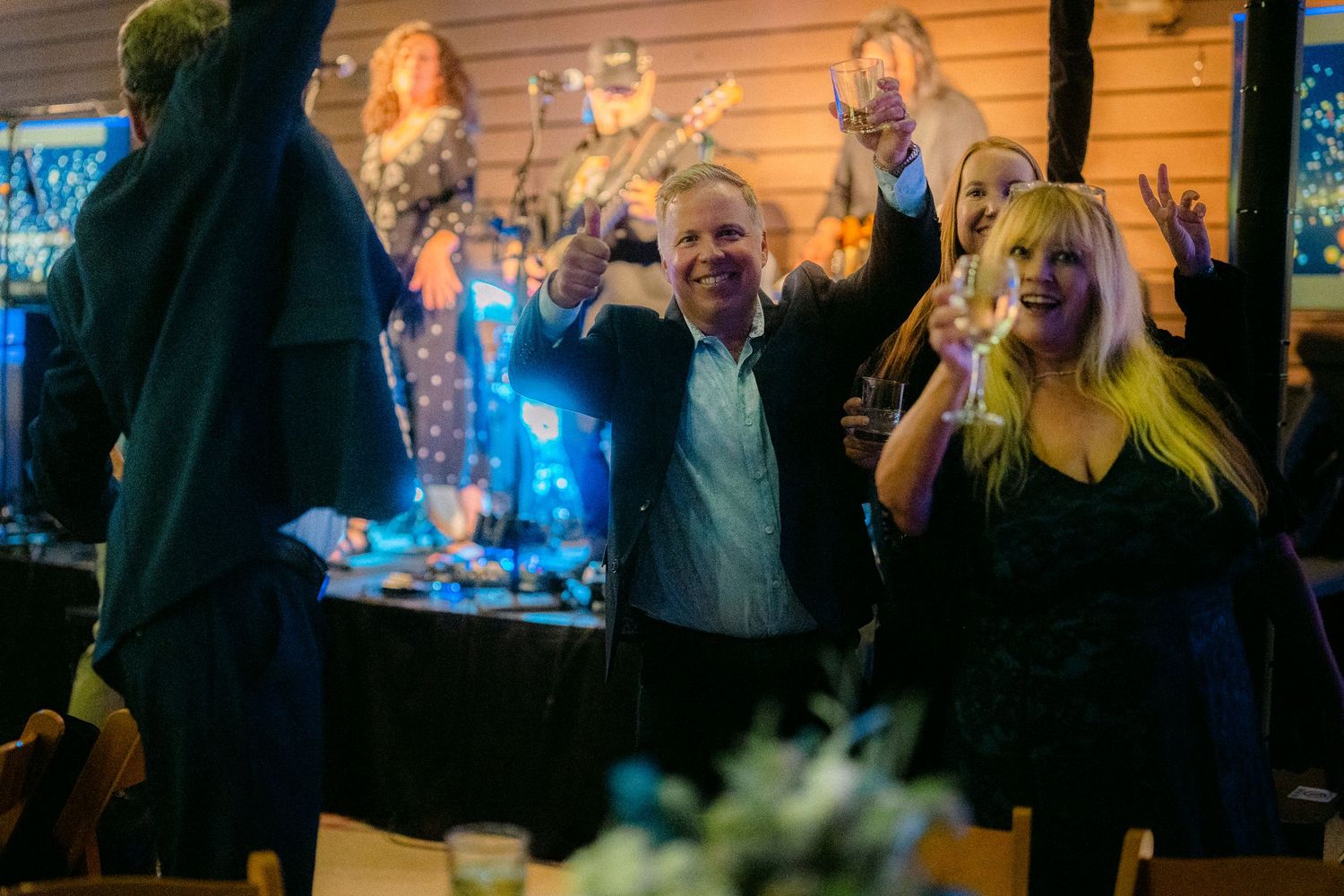 Guests celebrating at a lively party, raising glasses and cheering with colorful decorations in the background.