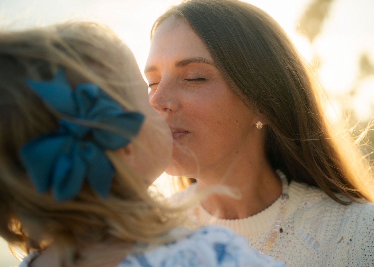 Mother and young daughter sharing a tender kiss in golden sunlight.