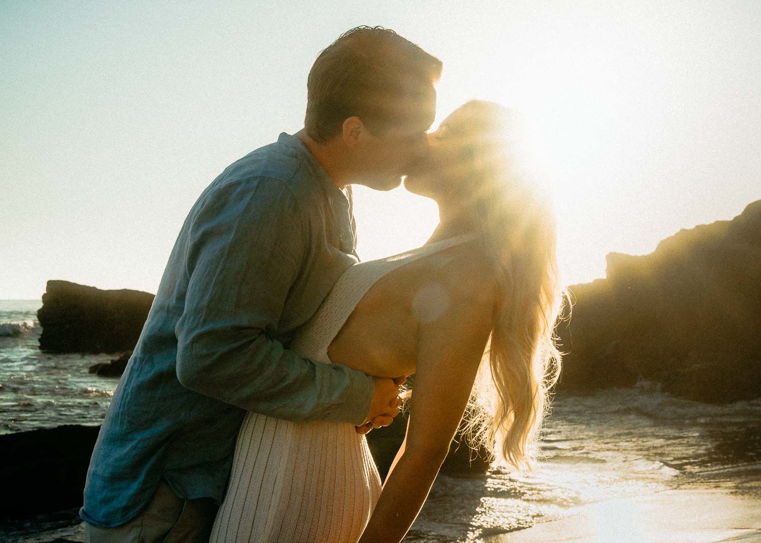 Couple sharing a kiss on the beach with warm golden sunlight.
