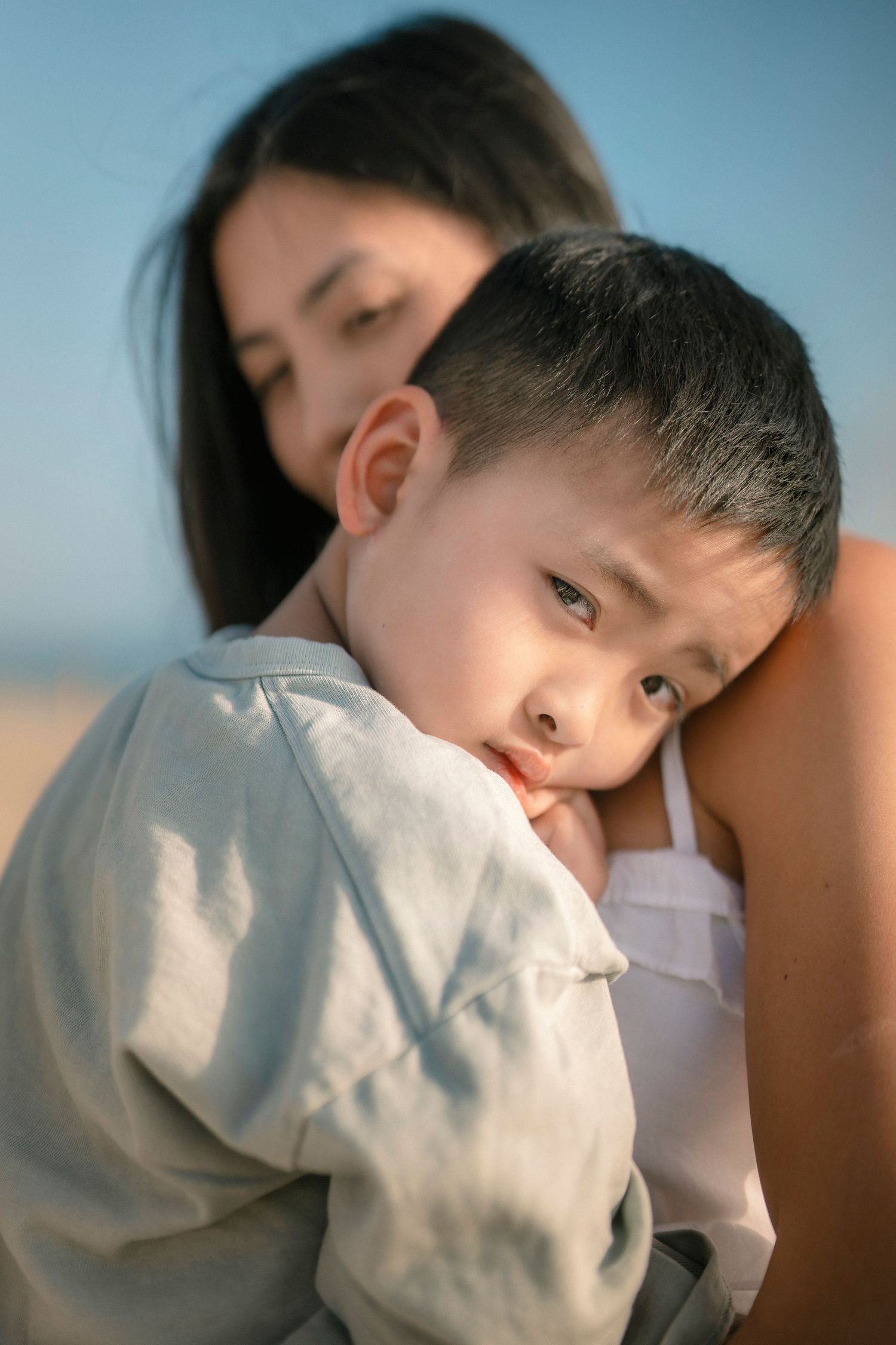 Young boy resting his head on a woman's shoulder during a tender beach moment.