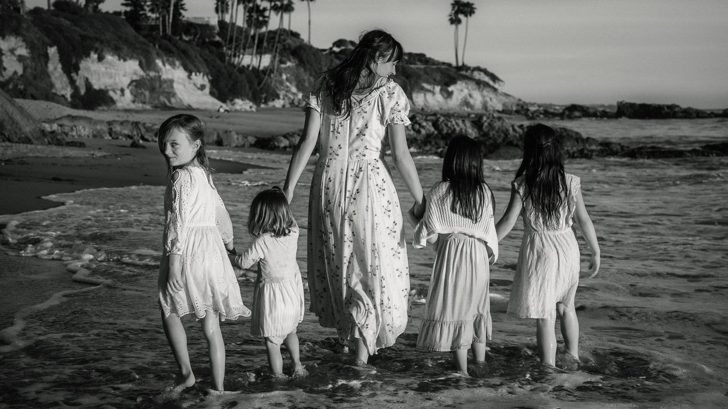 Black and white photo of mother walking on beach holding hands with four children.