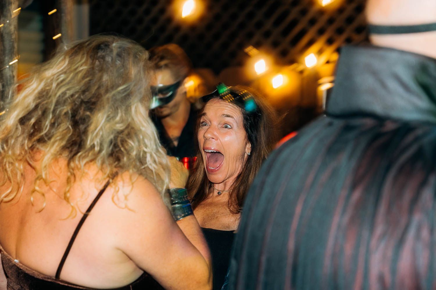 Excited woman with an open mouth expression socializing at a lively masquerade party.