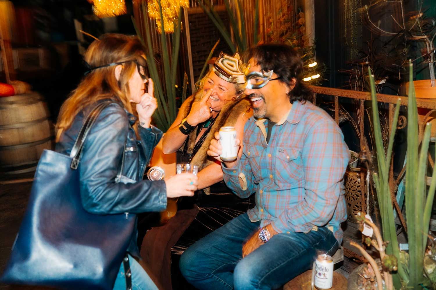 Three friends laughing and sharing drinks together outside at a casual night event.