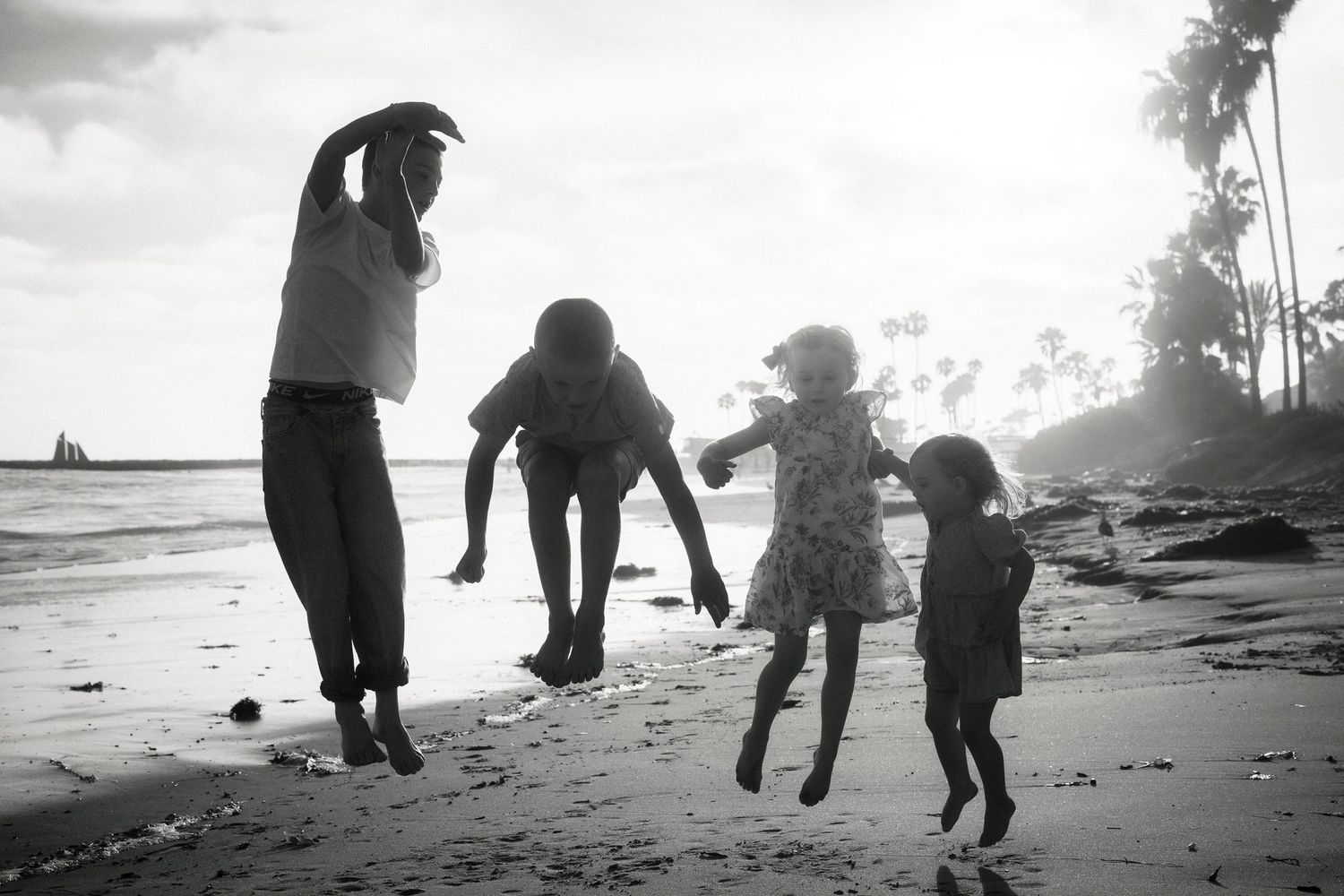 Black and white photo of a family playing on a tropical beach at sunset.