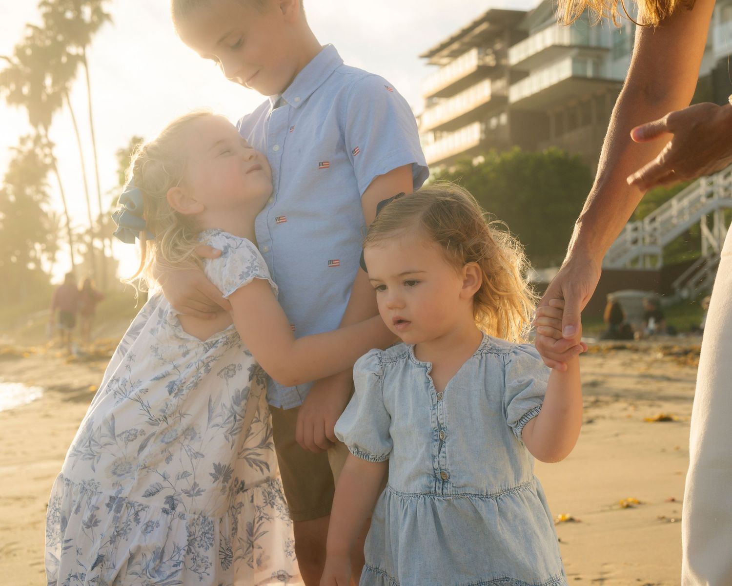 Three young children embracing on a golden sunset beach.