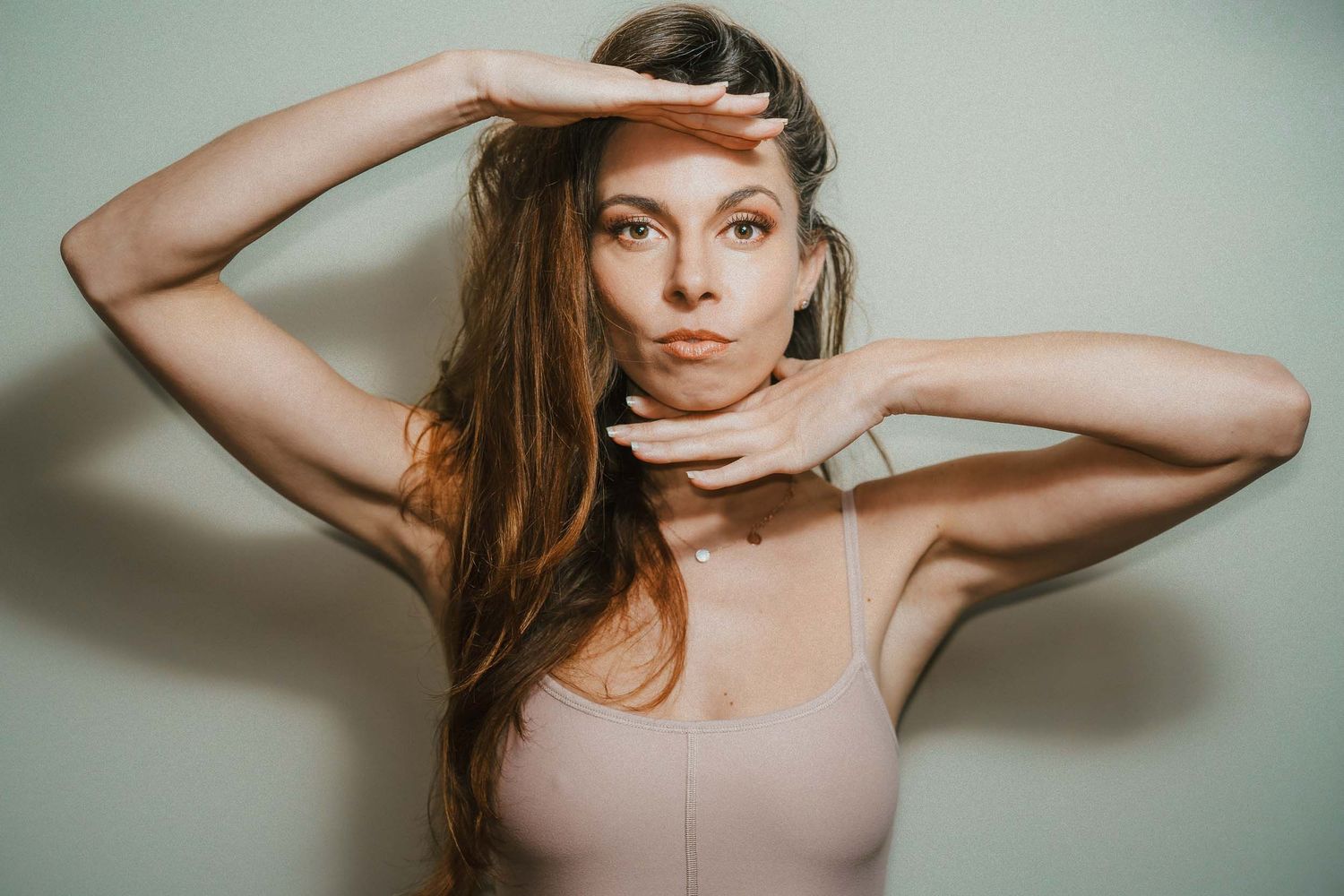 Young woman posing with hands framing her face against a neutral studio background.