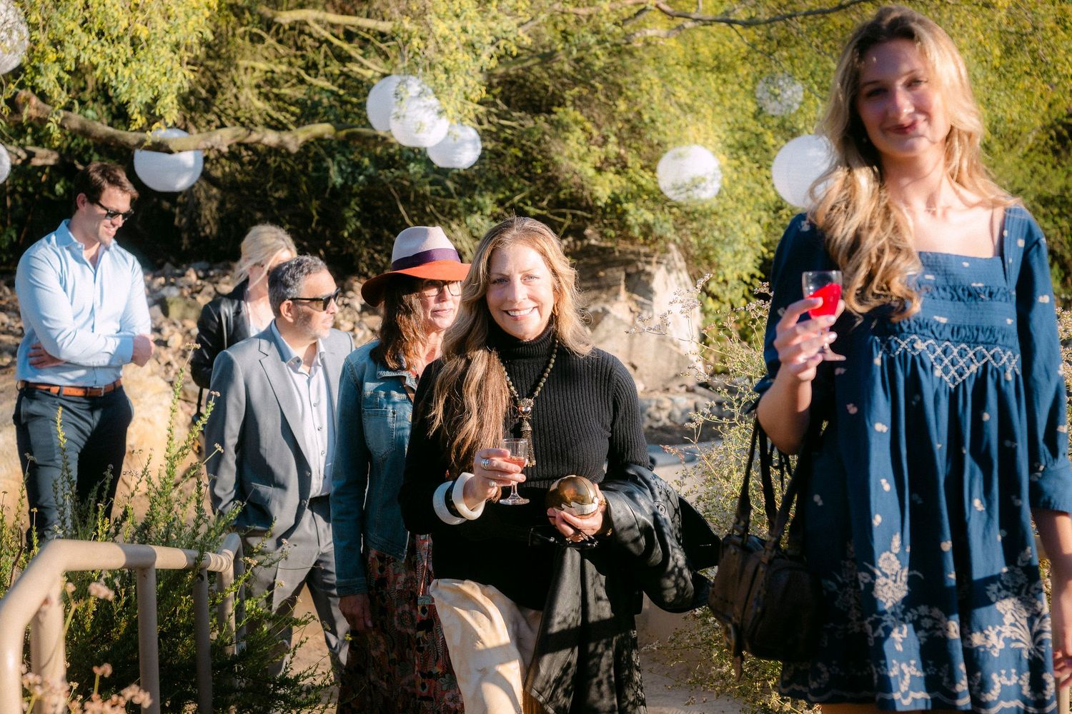 Guests walk through a lush garden path at an outdoor evening party with glowing balloon lights.