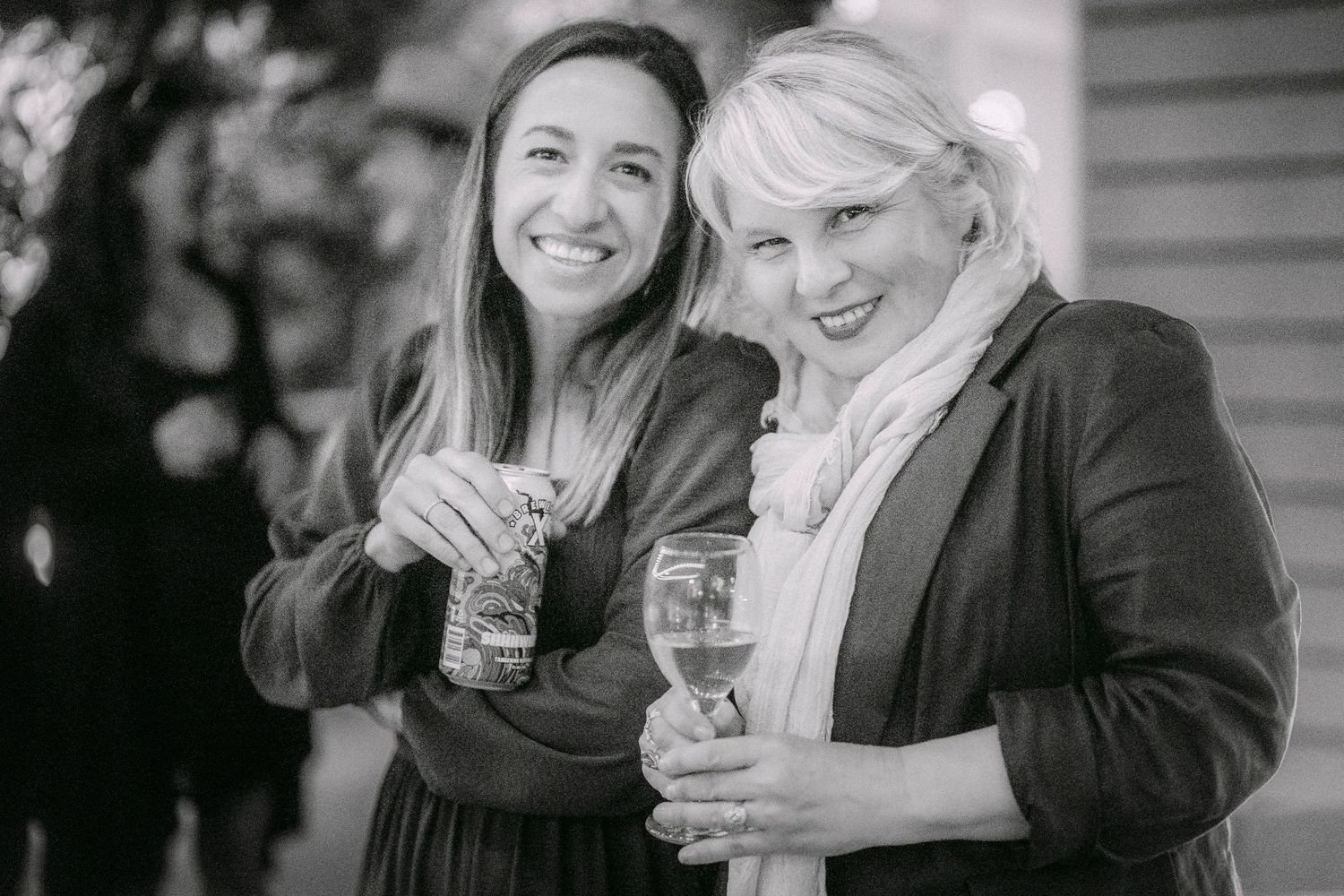 Two smiling women holding drinks at an outdoor social event in black and white photo.