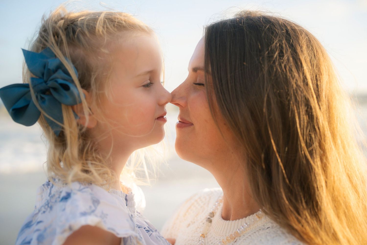 Mother and young daughter touching noses affectionately on a sunny beach.