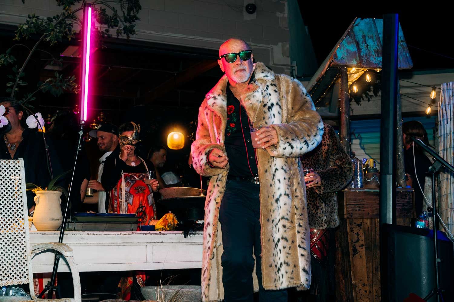 Man in a leopard fur coat performing on stage at an outdoor evening event.
